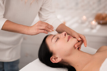 Professional massage therapist applying face massage to client