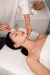 Crop beautician massaging face of female client with gua sha