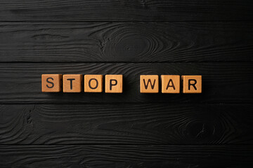 Wooden light yellow cubes with letters form the words Stop War on a black wooden table. Dark...
