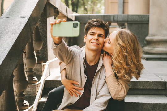 Cheerful man is taking a selfie of his girlfriend giving him a kiss on cheek.
