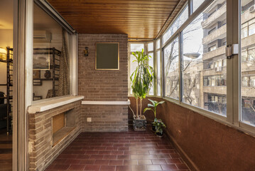 Fototapeta na wymiar A terrace with an aluminum and glass enclosure with brown stoneware floors, indoor plants and a dark brown brick wall