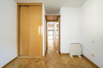 Empty room with a built-in wardrobe with oak sliding doors, plain white walls, an electric radiator and an oak laminate floor