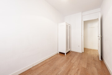 Empty room with white cabinet, white walls and laminated oak flooring
