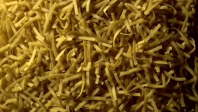 Uncooked Tagliatelle Lungo pasta rotating in fast motion - top view, flat lay, low key, food background. Raw dried organic golden long macaroni texture. Italian food, cuisine and culture close up