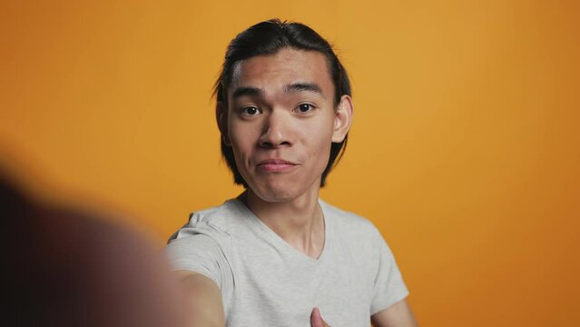 POV of asian smiling man taking pictures on camera, acting funny and silly over orange background. Cheerful casual model posing for photos in studio, smiling and being happy. Carefree hipster.