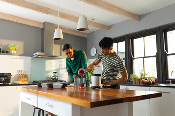 Diverse gay male couple preparing juice together in the kitchen at home