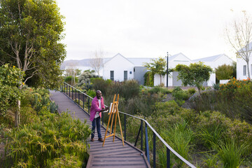 African american senior man painting on easel on the garden pathway outdoors