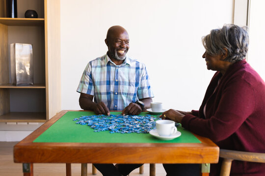 African american senior couple smiling while solving jigsaw puzzle at home