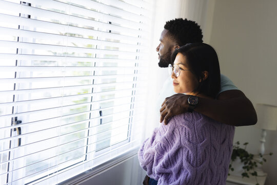 Happy diverse couple embracing and looking through window