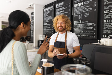 Happy diverse woman and male barista taking order in cafe
