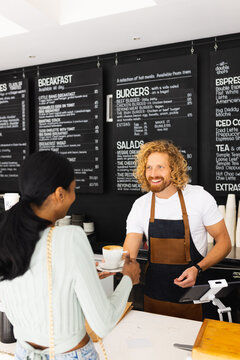 Happy diverse male barista and woman ordering cup of coffee in cafe