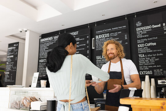 Happy diverse male barista and woman ordering cup of coffee in cafe