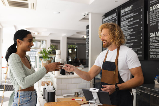 Happy diverse male barista and woman ordering cup of coffee in cafe