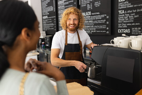 Happy diverse woman and male barista preparing coffee in cafe