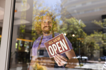 Happy caucasian male barista wearing apron and opening cafe