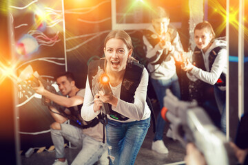 Emotional girl with laser pistol playing laser tag with friends on dark labyrinth..