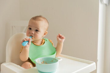 baby 1 year old eats baby food from a spoon sitting at the table, the first complementary foods and healthy food for small children.