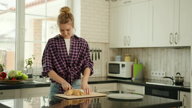 Caucasian woman in a plade shirt cutting wheat bread on a wooden board and putting the slices on a plate. Slow motion of a woman making sandwiches in her kitchen. High quality 4k footage