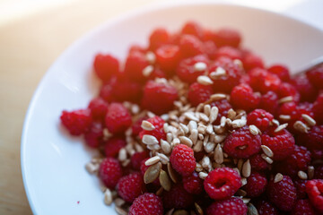 fresh red healthy raspberry with sunflower seed in white plate, wood background