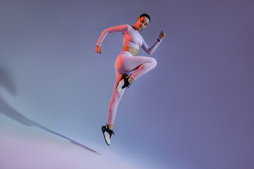Fototapeta na wymiar Athletic active woman jumping on studio background with colored filter. Dynamic movement