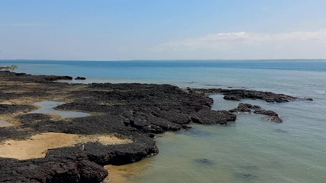 Image of a beach at low tide with blue and calm water, golden sand and dark rock, a paradisiacal and beautiful beach