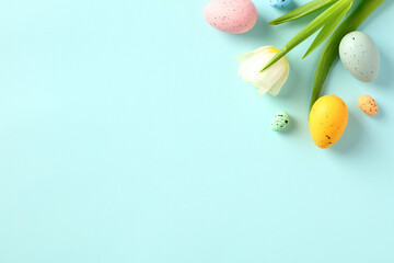 Happy Easter concept. Colorful Easter eggs with tulips on light blue background. Flat lay, top view, copy space.