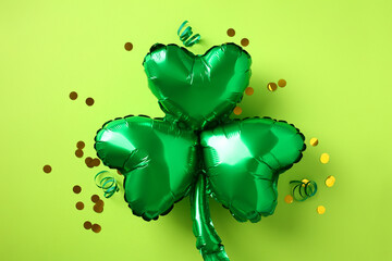 Green shamrock shaped balloon with confetti on light green background. Flat lay, top view.