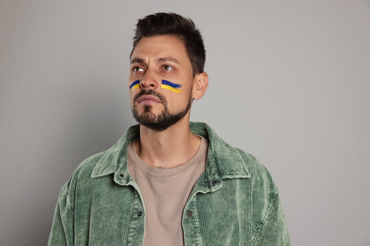 Man with drawings of Ukrainian flag on face against light grey background