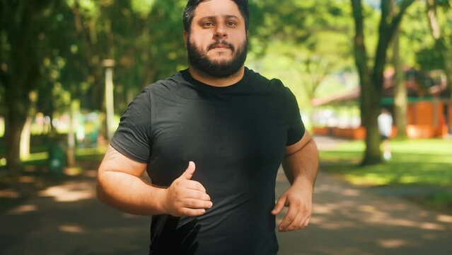 Young overweight man jogging at the park on a sunny summer day in slow motion