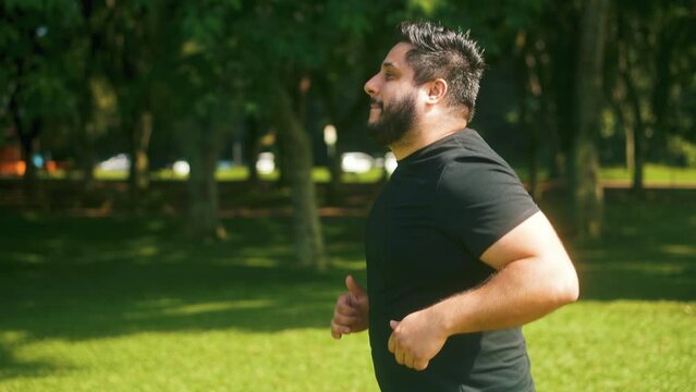 Happy overweight young man jogging outdoors on sunny day