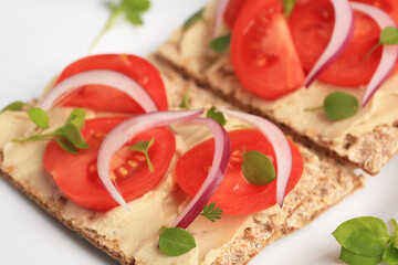 Fototapeta na wymiar Fresh crunchy crispbreads with pate, tomatoes, red onion and greens on white plate, closeup