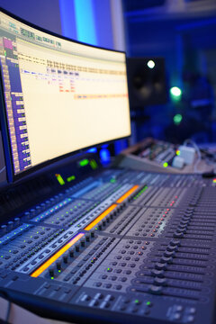 Producer / Sound Engineer creating and editing a song on an audio console with a screen displaying the track on top. Shot in an indoor music studio with blue and purple ambient lighting.