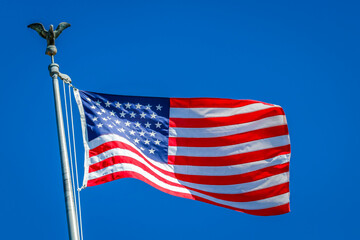 Obraz premium American flag waving on pole with eagle and bright colors against blue sky