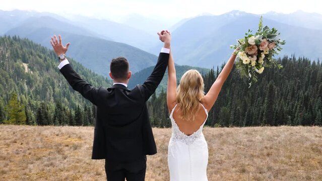 Happy groom and bride at their wedding in the mountains. They raise their hands and celebrate their happiness. Slow motion.