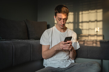 A young guy is using his mobile phone while sitting on the ground in his room