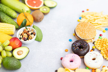 Flat lay of Healthy and unhealthy food from fruits and vegetables vs fast food, sweets and pastry on gray concrete background. Diet and detox against calorie and overweight lifestyle concept.