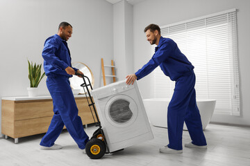 Male movers carrying washing machine in bathroom. New house