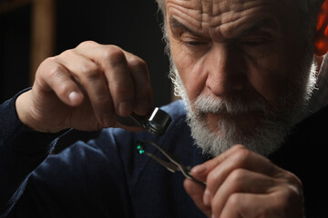 Professional jeweler working with gemstone on dark background, closeup