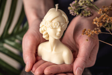 Hands carefully hold a beautiful white handmade candle in the shape of a female body