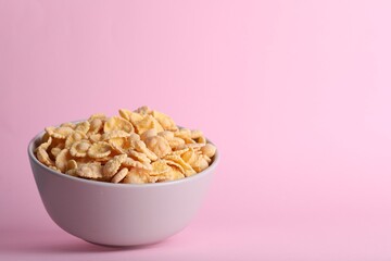 Bowl of tasty crispy corn flakes on pale pink background, space for text