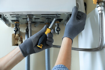 Man repairing gas boiler with screwdriver indoors, closeup