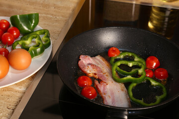 Cooking bacon with tomatoes and pepper in frying pan. Ingredients for breakfast