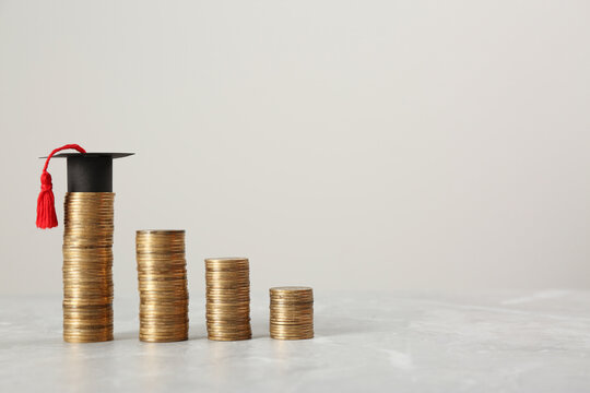 Scholarship concept. Graduation cap and stacked coins on light grey table, space for text