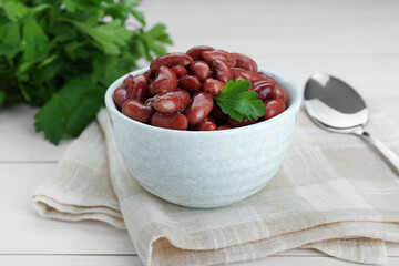 Bowl of canned kidney beans with parsley on white wooden table, closeup