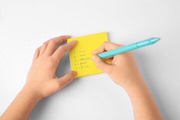 Child erasing words and numbers written with erasable pen on white background, top view