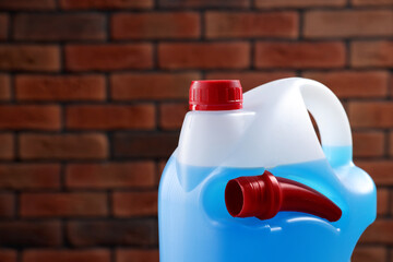 Plastic canister with blue liquid against brick wall, closeup. Space for text
