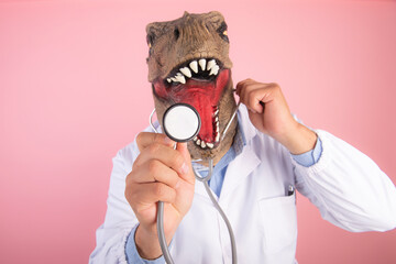 doctor with T Rex mask holding a stethoscope close-up on an isolated pink background. selective...