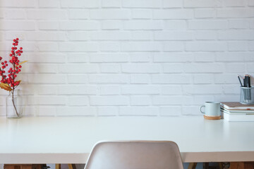 Home office desk with books, cup of coffee and stationery on white table against brick wall. Copy space for your text.