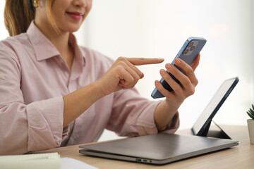 Cropped shot of smiling asian woman employee sitting at office desk and using smart phone.