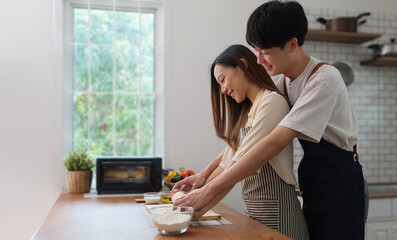 Beautiful young couple preparing meal, making fresh dough for breakfast in the kitchen .